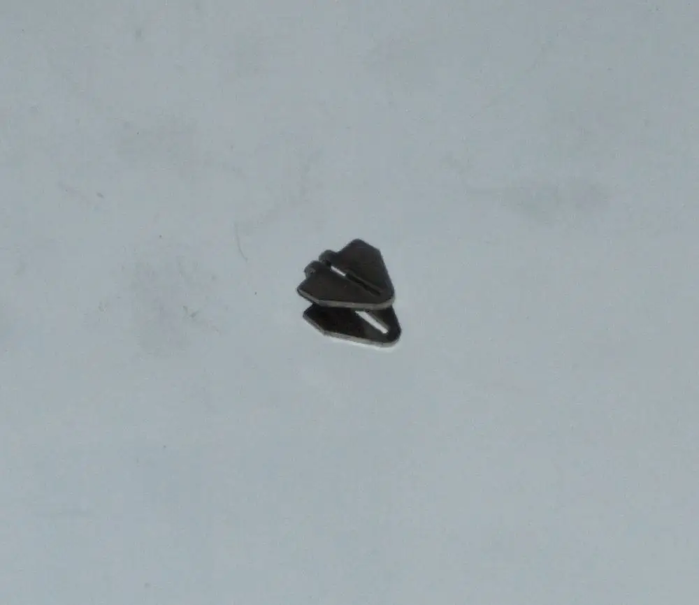 Schwarze Abstandsklammer von Daikin, platziert auf einem glatten Untergrund. Die Klammer hat eine symmetrische Form mit zwei überlappenden Teilen.